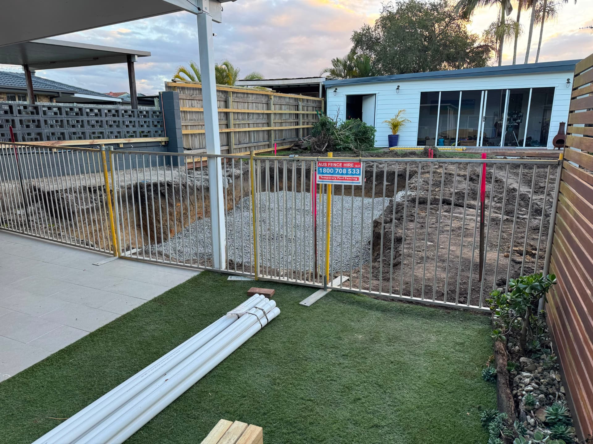 Temporary pool fencing around a backyard pool excavation at dusk